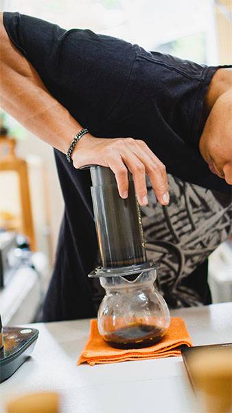 Someone squeezing Aeropress Coffee into a jug, on the top of Bean Merchant's how to make Aeropress Coffee website